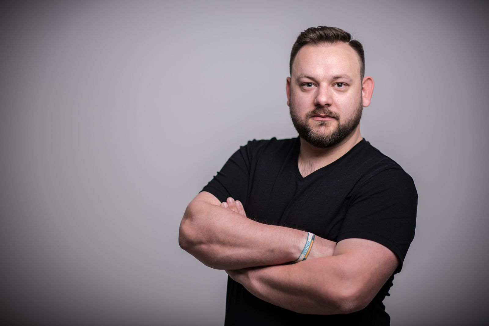 Christian Reichinger im schwarzen T-Shirt mit verschränkten Armen vor grauem Studiohintergrund